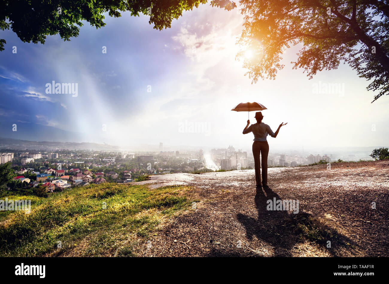 Silhouette di donna con ombrello la strada con vista sul panorama della città in piovoso tramonto spettacolare . Vintage, in stile retrò. Foto Stock