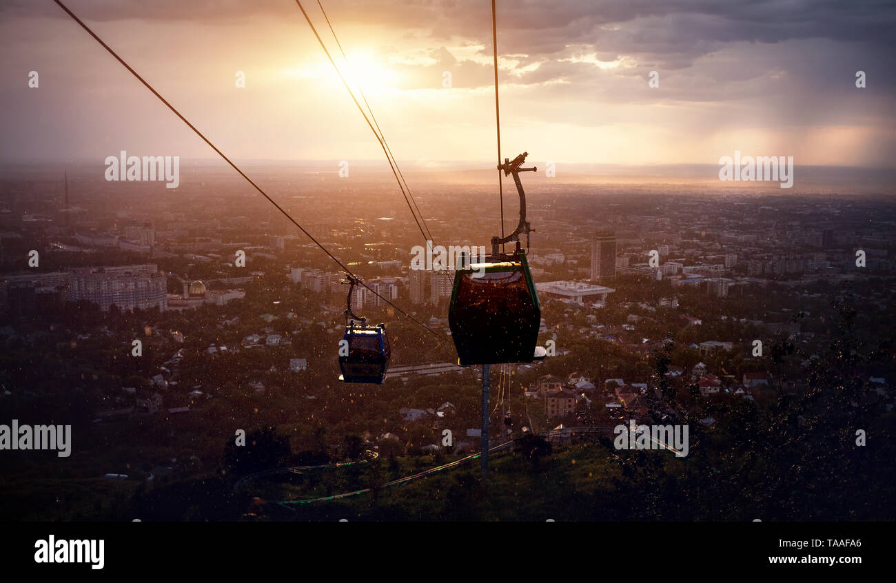 Silhouette di funivia in vista della città al drammatico tramonto tempestoso sullo sfondo del cielo Foto Stock