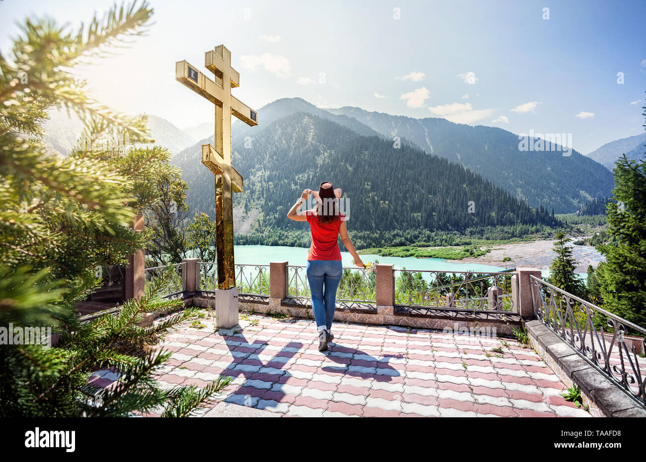 Tourist donna con cappello godendo di una splendida vista del lago di montagna nelle montagne vicino al grande croce dorata in Kazakistan Foto Stock