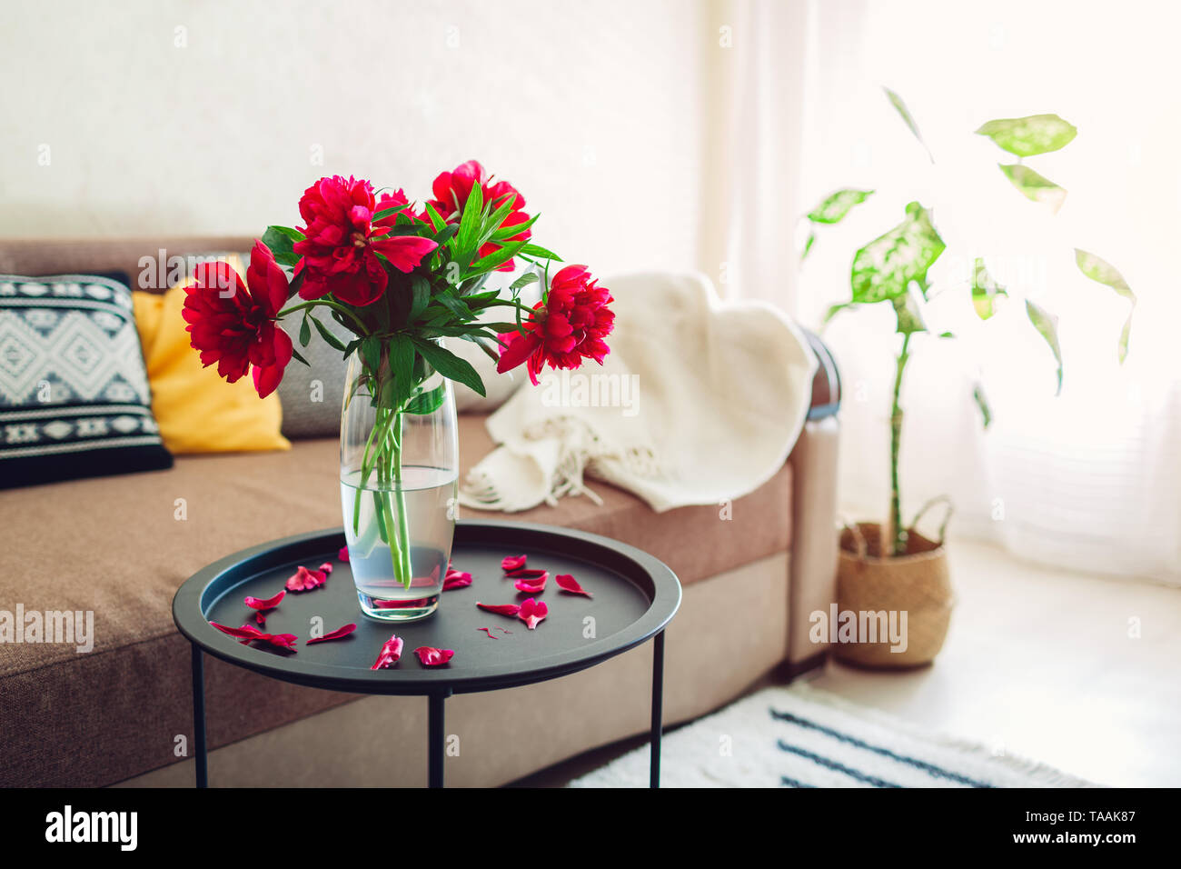Interno della sala decorata con le peonie fiori, piante e tappeti. Accogliente lettino con cuscini e tavolo Foto Stock