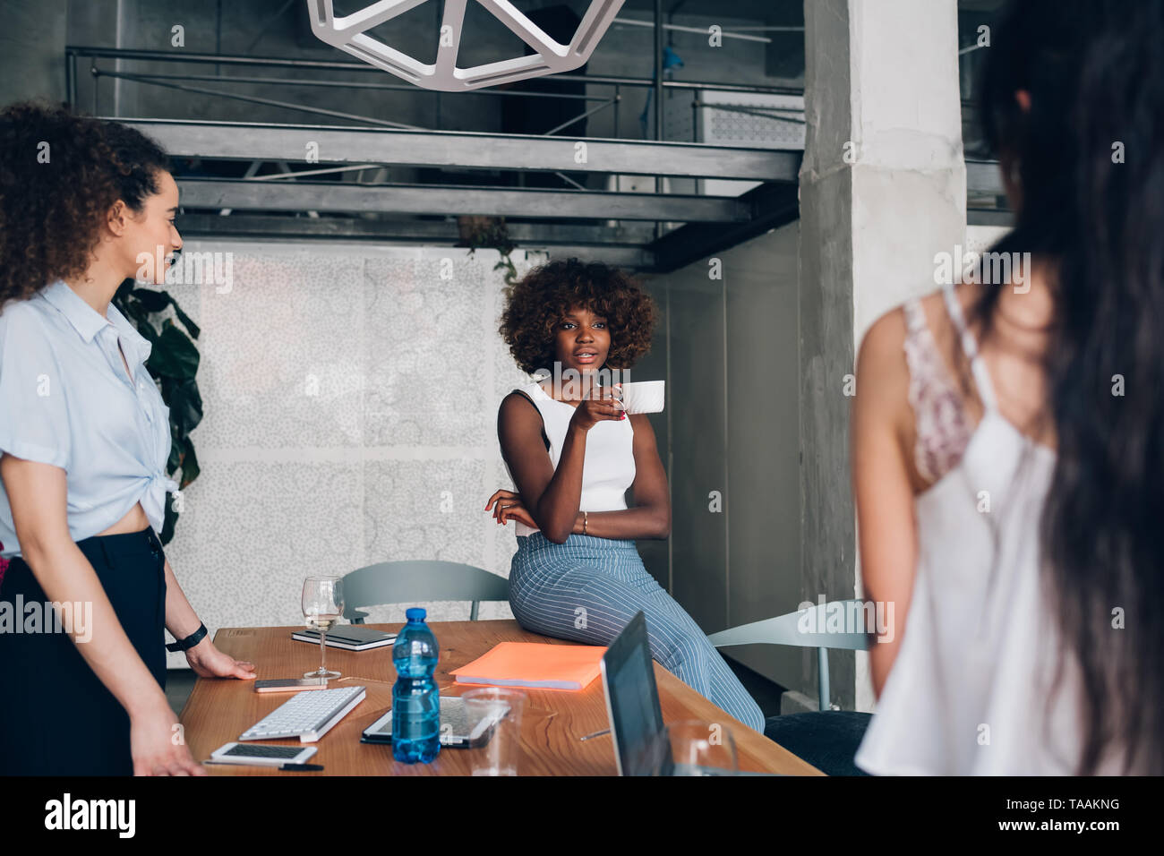 Tre giovani multirazziale freelancer donna avente una riunione informale in coworking office - interazione, creatività, tecnologia Foto Stock