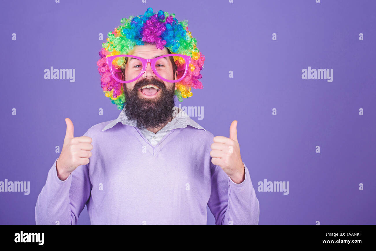 Vestita a festa di compleanno. Uomo di moda parrucca gesticolando Thumbs up. Uomo Barbuto in parrucca clown acconciatura. Hipster uomo che indossa rainbow parrucca capelli. Felice l'uomo con la barba lunga e il ricciolo parrucca, copia dello spazio. Foto Stock
