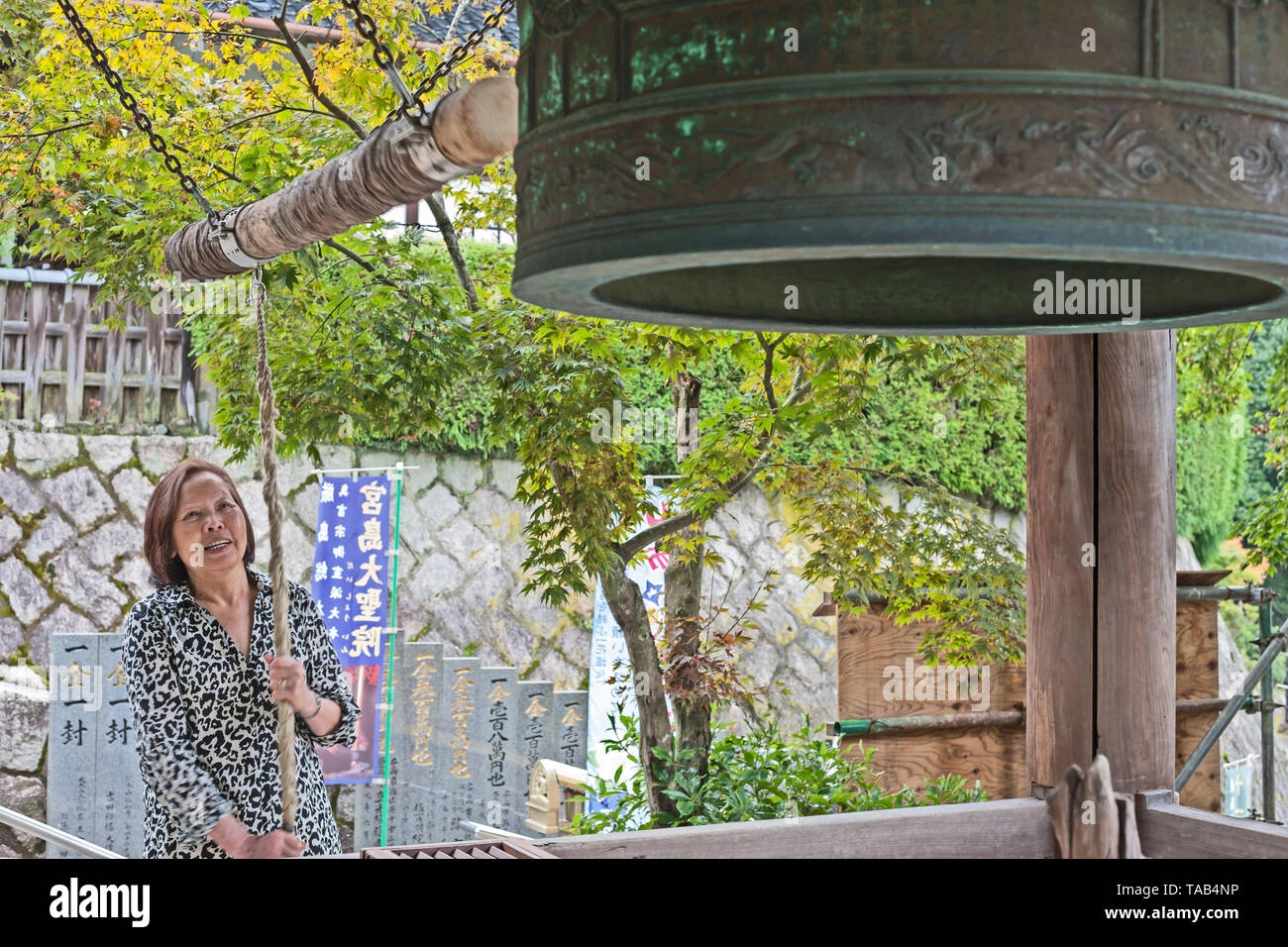 Asian Lady tirando la corda per suonare il campanello al Belfry presso il tempio Daishoin, l'isola di Miyajima, Giappone Foto Stock