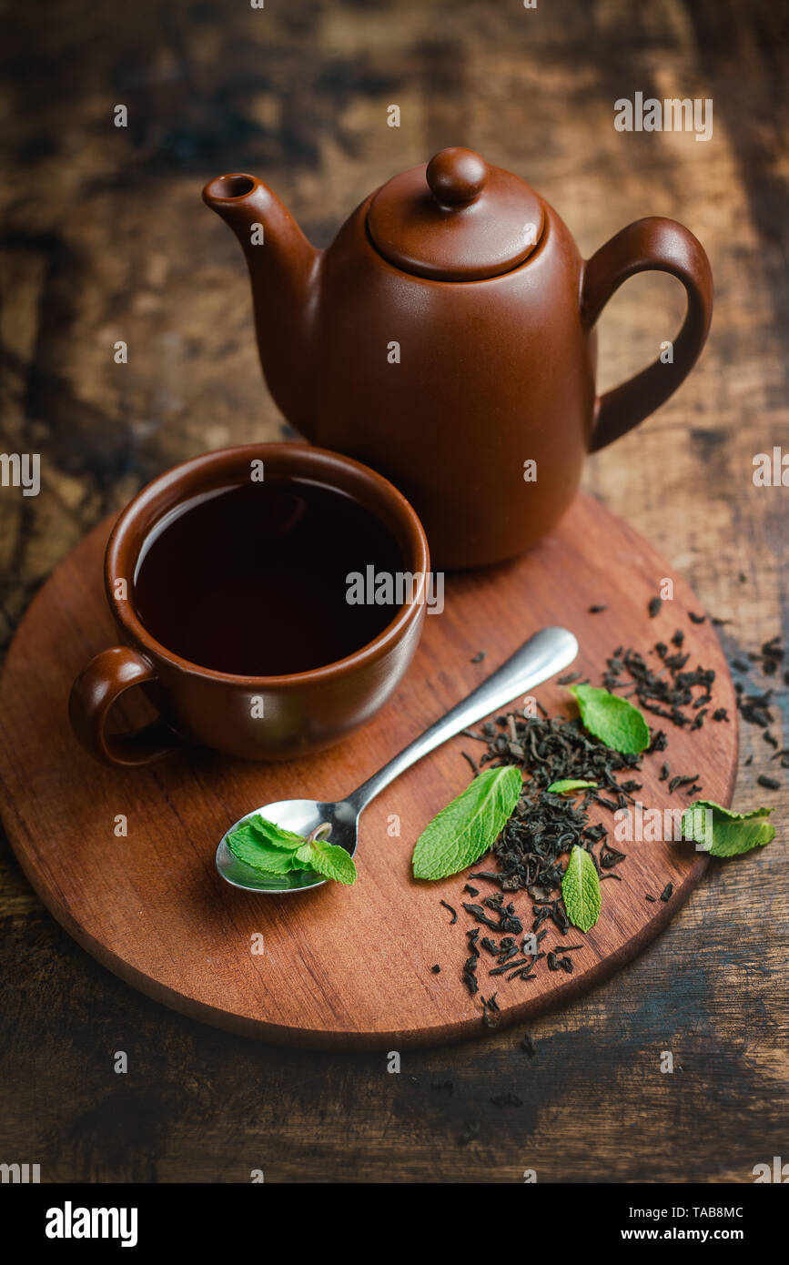 Il tè alla menta in marrone tazza di ceramica e teiera su un caldo sullo sfondo di legno con infuso di tè e foglie di menta. Foto Stock