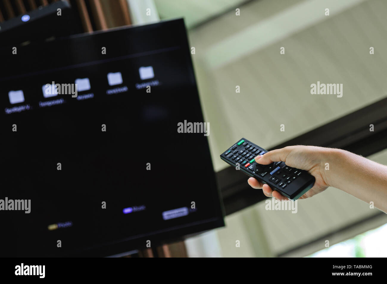 Mano femminile con il telecomando del televisore selezionando una cartella sulla schermata Foto Stock