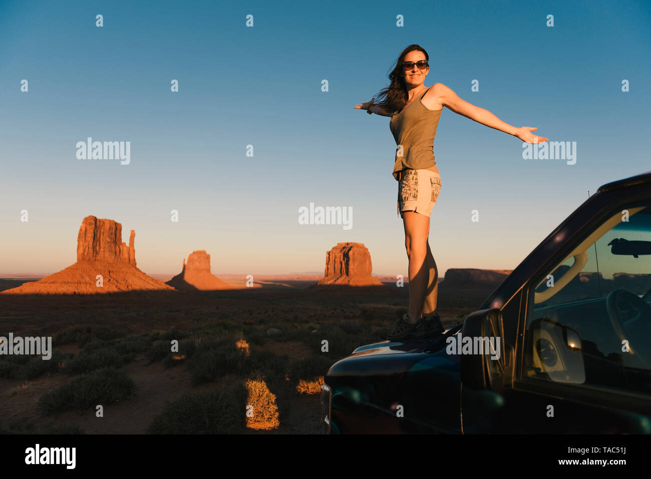 Stati Uniti d'America, Utah, Monument Valley, donna in piedi sul cofano auto, godendo del tramonto nella Monument Valley Foto Stock