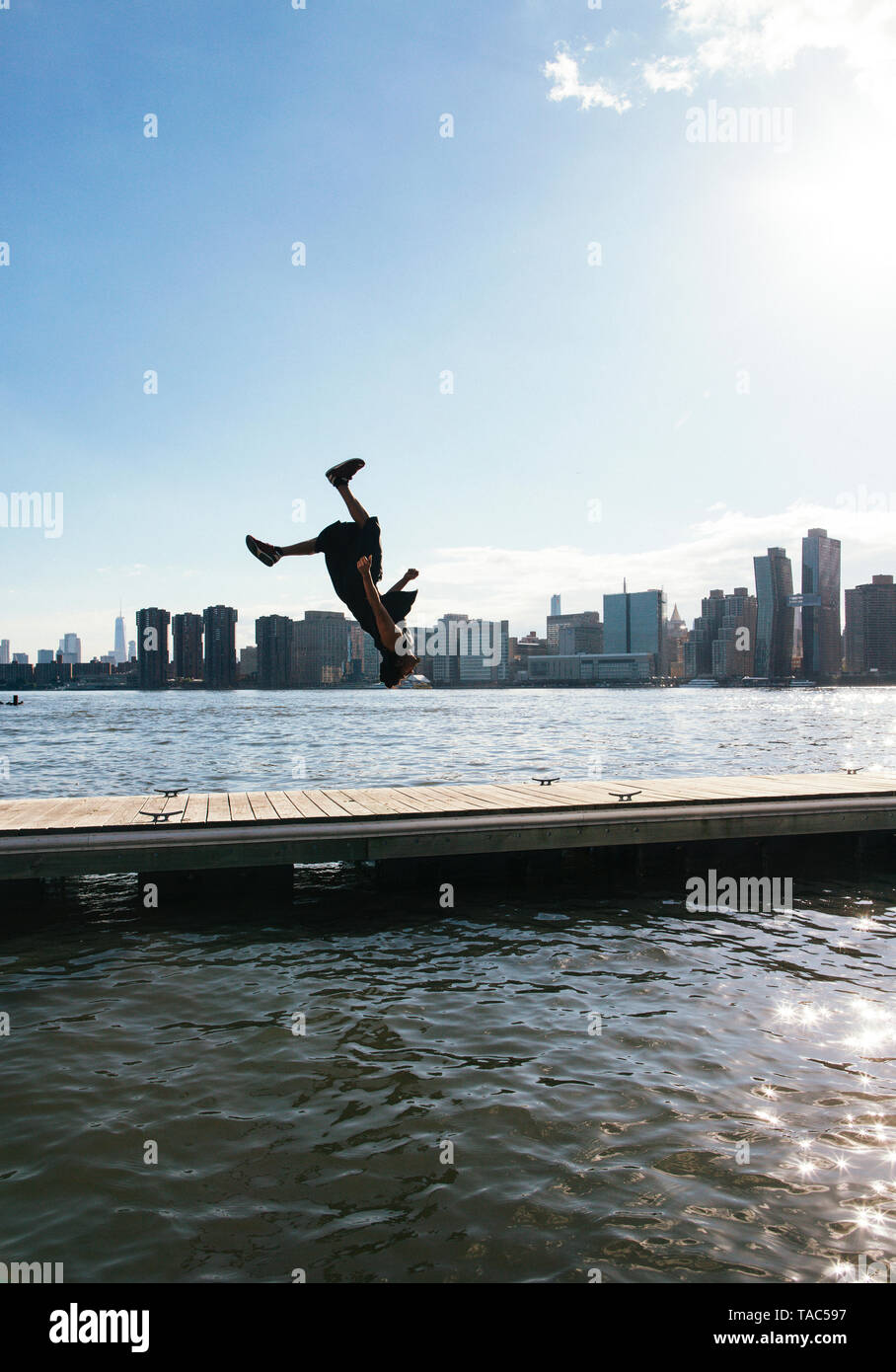 Stati Uniti d'America, New York, Brooklyn, giovane uomo facendo backflip sul molo di fronte skyline di Manhattan Foto Stock