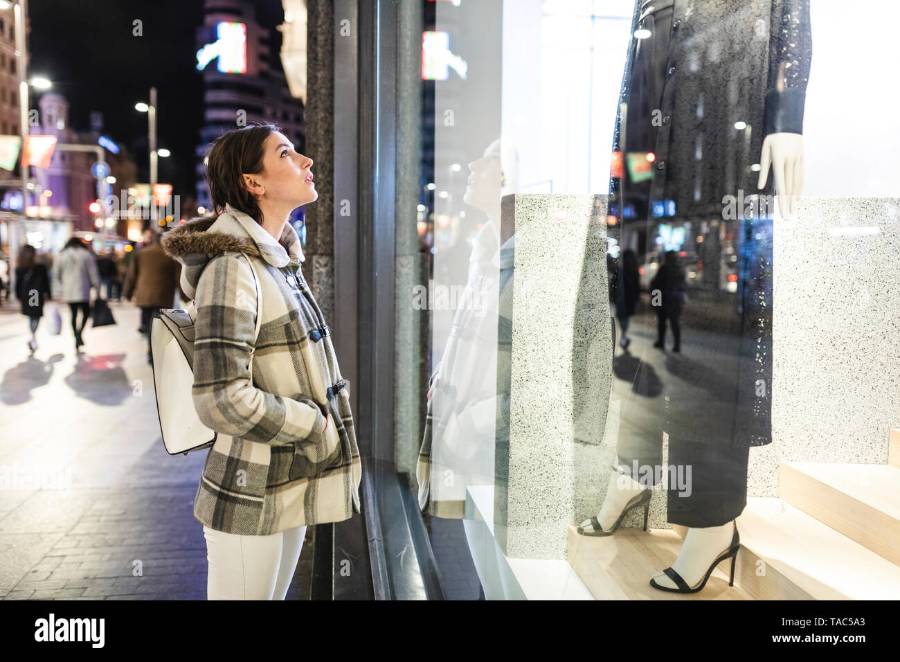 Spagna, Madrid, giovane donna nella città di notte accanto alla Gran Via guardando una finestra shop Foto Stock