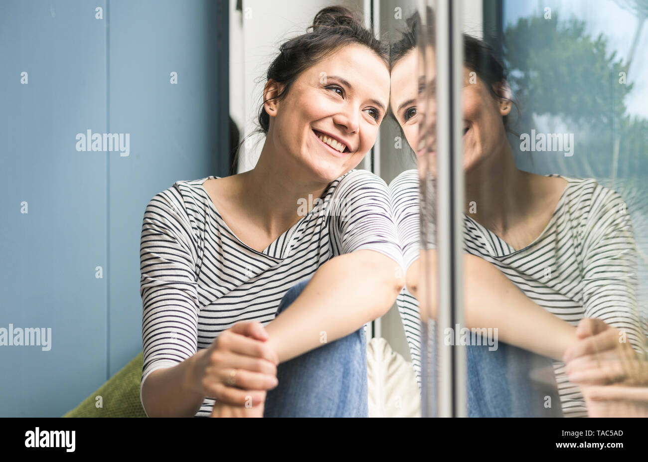 Donna sorridente guardando fuori della finestra a casa Foto Stock