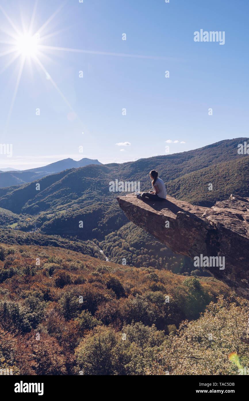 Spagna, Navarra, foresta di Irati, donna seduta su sperone di roccia sopra paesaggio forestale in controluce Foto Stock