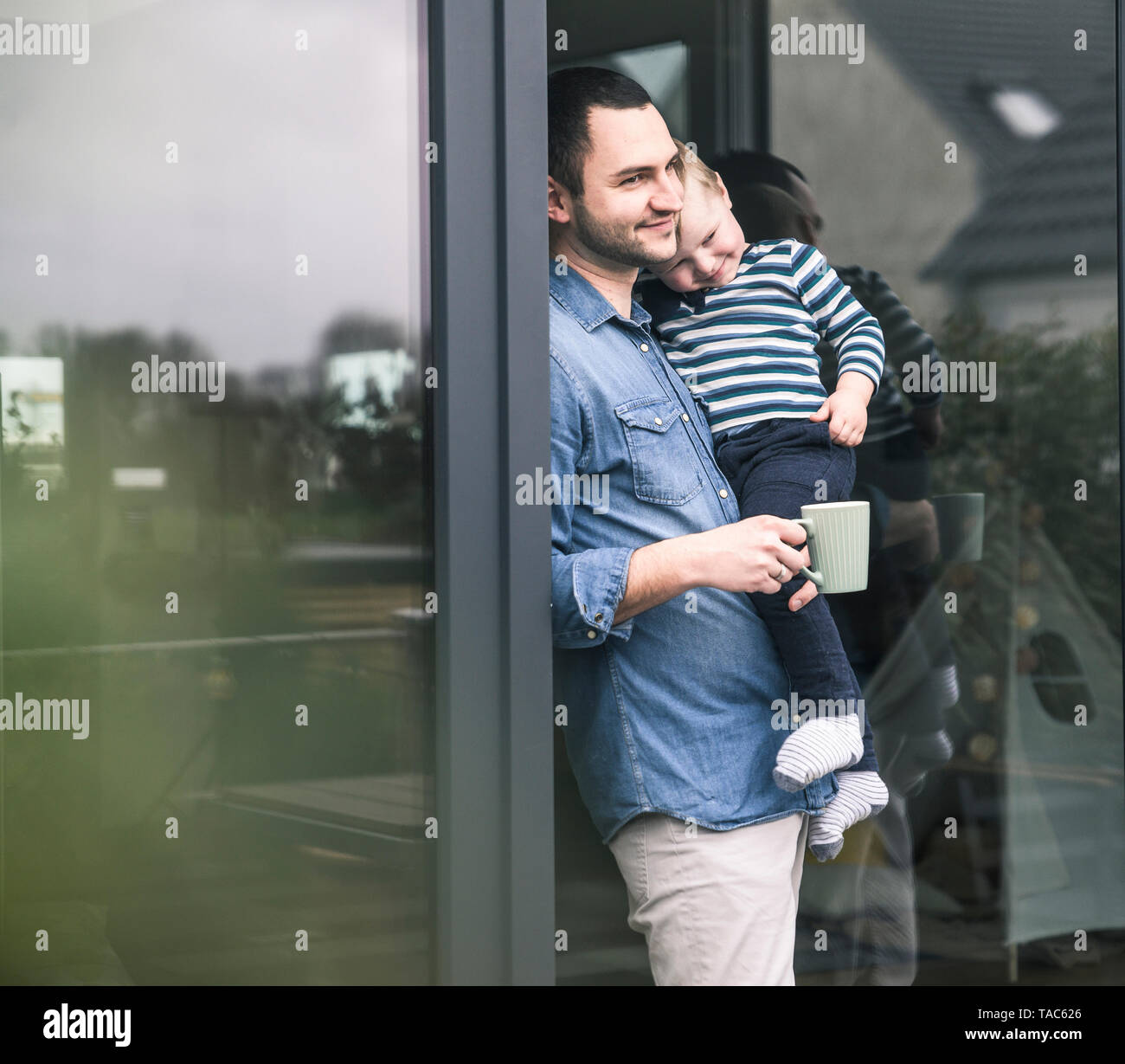 Padre con la tazza di caffè che porta il figlio a terrazza o porta a casa Foto Stock