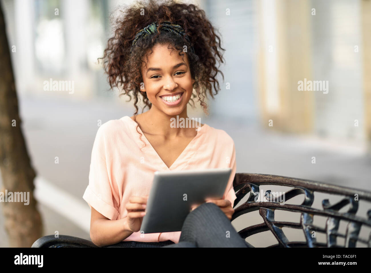 Ritratto di felice giovane donna seduta su una panchina con tablet Foto Stock