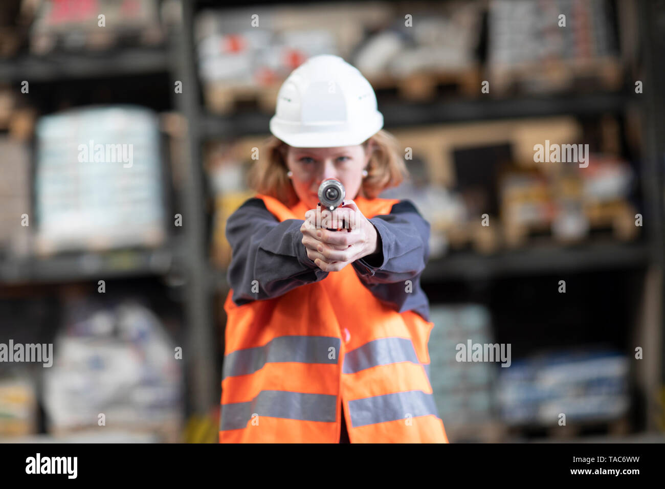 Donna che indossa giubbotto ed elmetto holding trapano portatile come una pistola Foto Stock