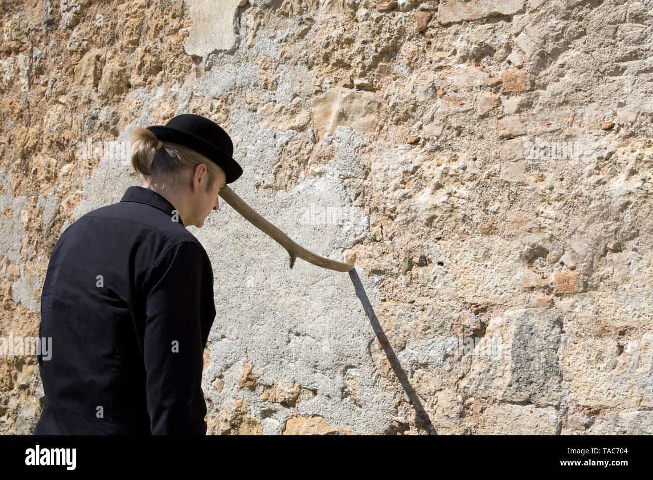 Uomo che indossa un cappello bowler equilibratura di un bastone a un muro di pietra Foto Stock