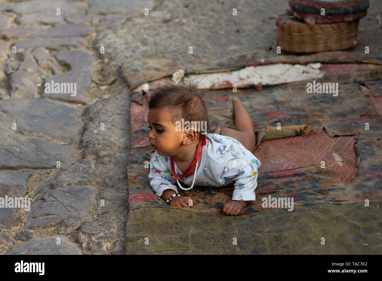 Piccolo bambino indiano che stabilisce su stracci in strada con il nero eyeliner e cravatta rossa Foto Stock