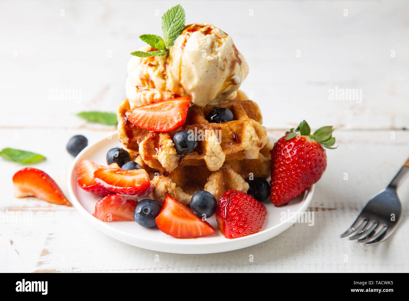Pila di cialde con more di rovo e fragole, gelato alla vaniglia e caramello sciroppo su un bianco tavolo in legno Foto Stock