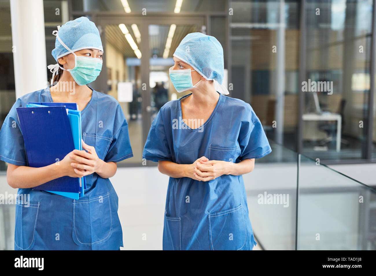 Due chirurghi in blu camici chirurgici e con maschere chirurgiche di fronte alla sala di emergenza Foto Stock