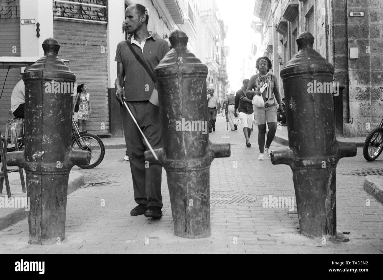Un uomo cieco con bastone bianco fa il suo modo in passato canon bloccato nel terreno nella Vecchia Havana, Cuba Foto Stock