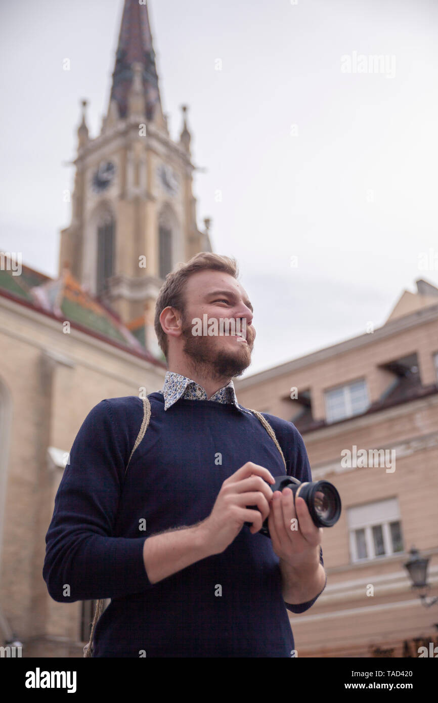 Un giovane uomo sorridente, il turista o il viaggiatore in possesso di una fotocamera, in un vecchio stile Europeo città architettura in background. Foto Stock