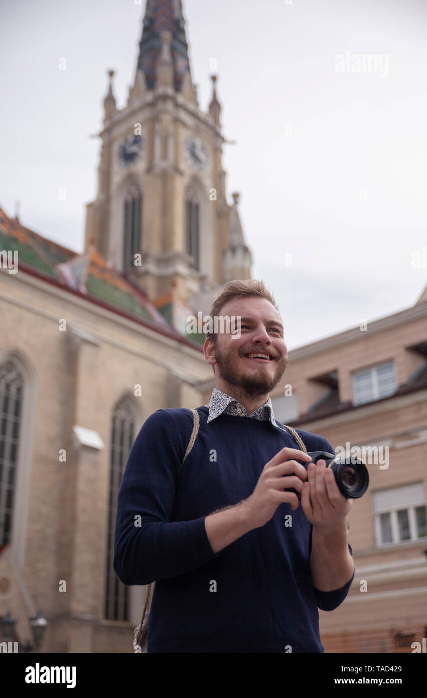 Un giovane uomo sorridente, il turista o il viaggiatore in possesso di una fotocamera, in un vecchio stile Europeo città architettura in background. Foto Stock