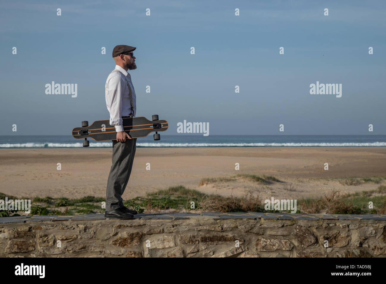 Uomo con longboard in piedi su una parete di fronte spiaggia e mare Foto Stock