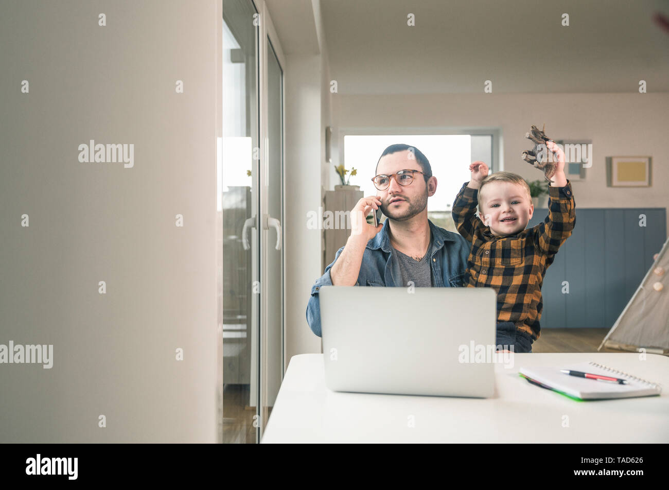 Padre lavora a tavola in casa ufficio con Figlio seduto sul suo giro Foto Stock