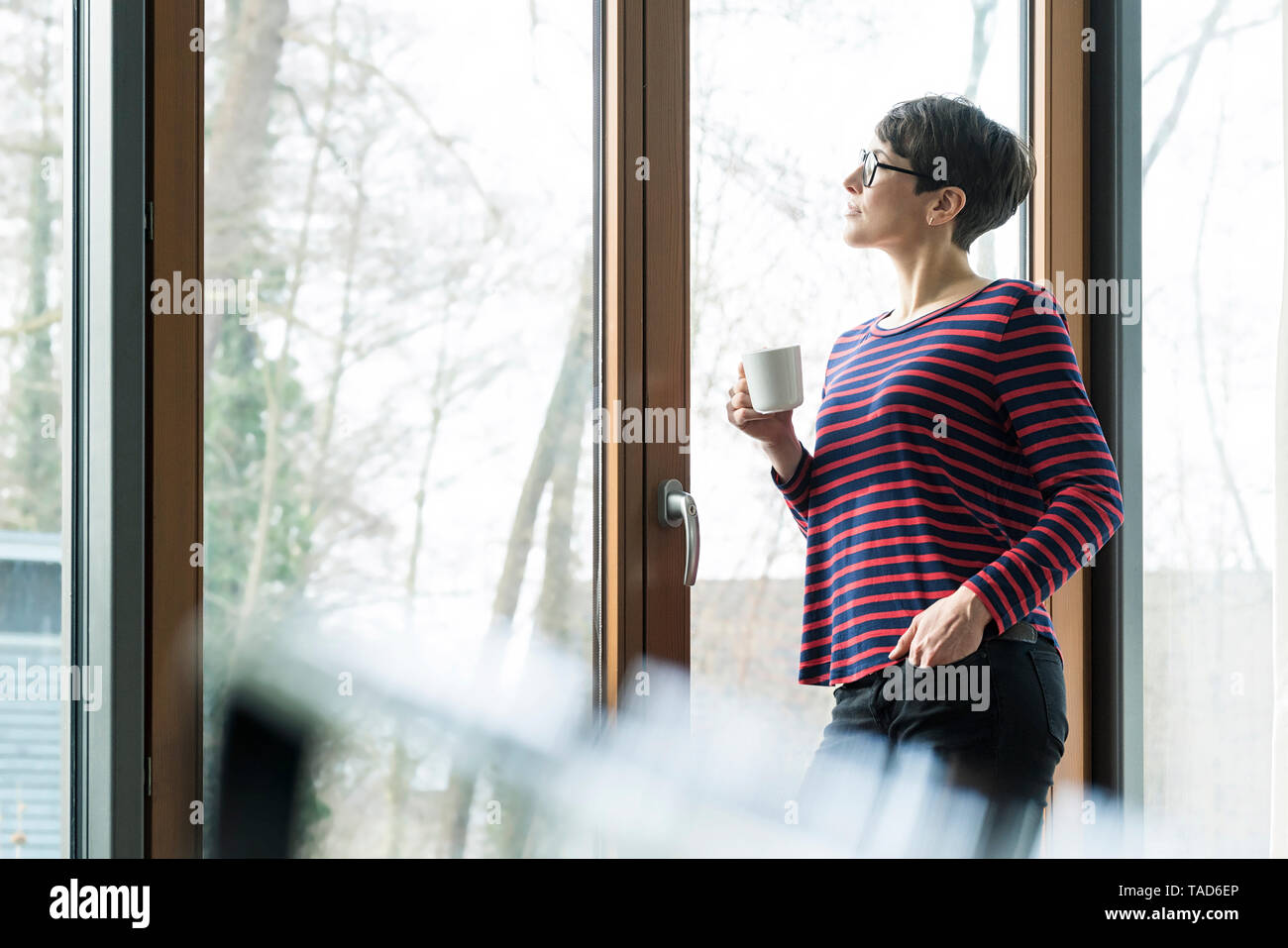 Donna con tazza da caffè guardando fuori della terrazza o porta Foto Stock