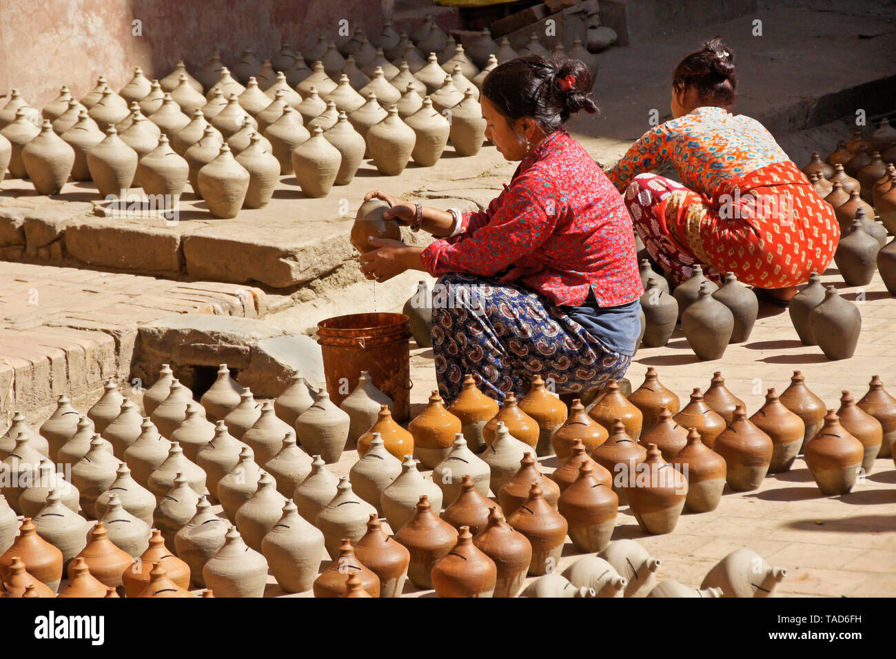 Le donne in ceramica di immersione nel colore come altri prodotti di creta sun-asciugare vicino Kumale Tol (Vasai Square, ceramica quadrato), Bhaktapur, Valle di Kathmandu, Nepal Foto Stock