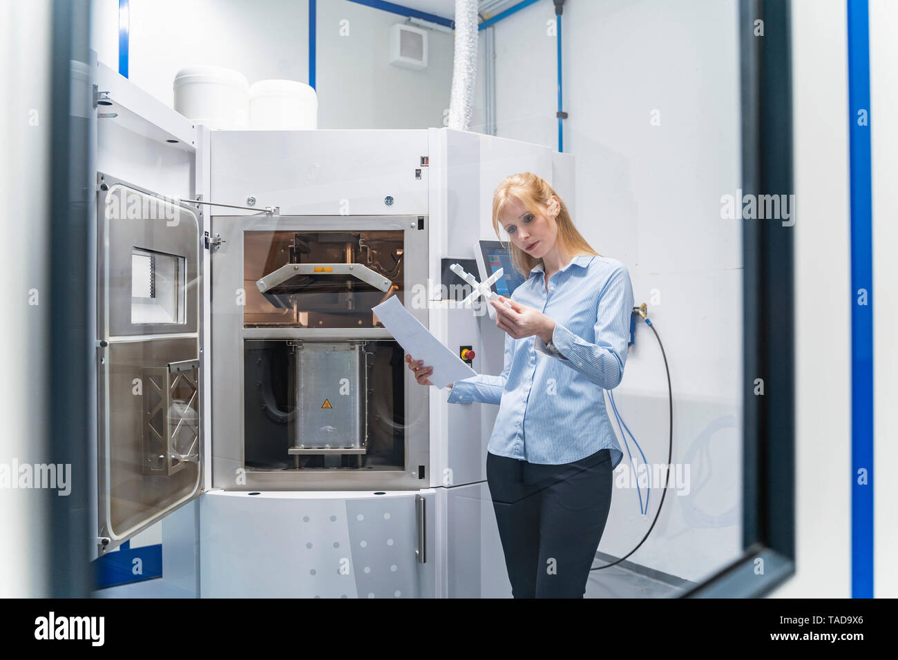Donna che mantiene la carta e il pezzo in lavorazione in corrispondenza stampante 3D Foto Stock