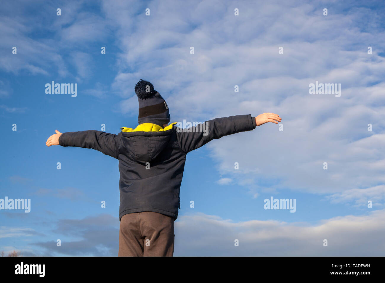 Un ragazzo da dietro a davanti a un cielo blu con bracci estesi Foto Stock