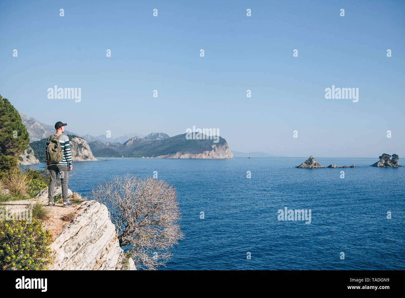 Un turista con lo zaino sulla cima di una scogliera o collina vicino al mare appare in lontananza. Viaggiare da soli. Foto Stock