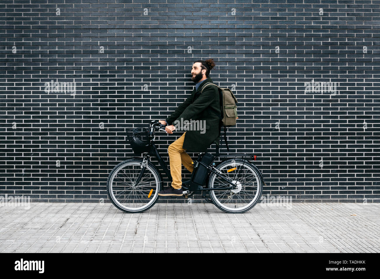 Uomo a cavallo e-bike lungo una parete di mattoni Foto Stock