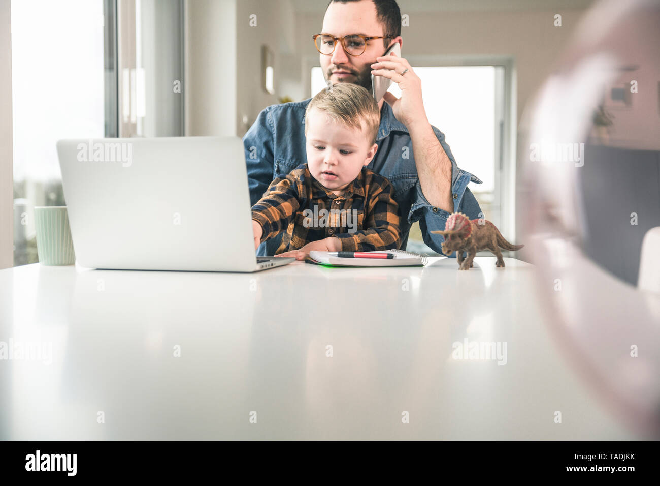 Padre lavora a tavola in casa ufficio con Figlio seduto sul suo giro Foto Stock