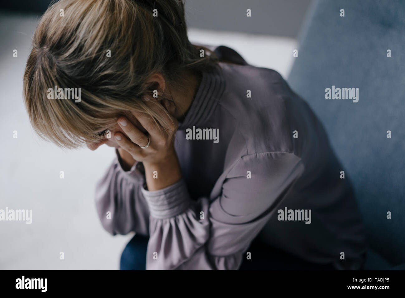 Triste donna seduta in poltrona con testa in mani Foto Stock