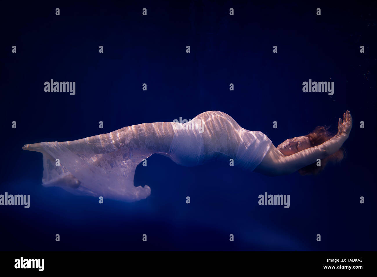 Donna incinta indossando abito bianco sotto l'acqua Foto Stock