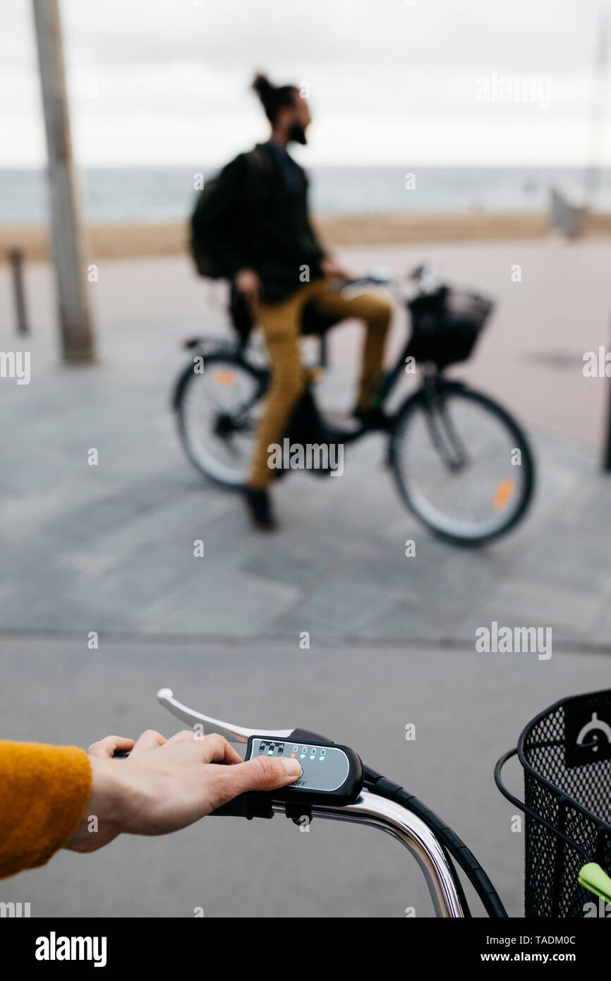 Close-up di donna su e-bike che collega il motore elettrico con l'uomo in background Foto Stock