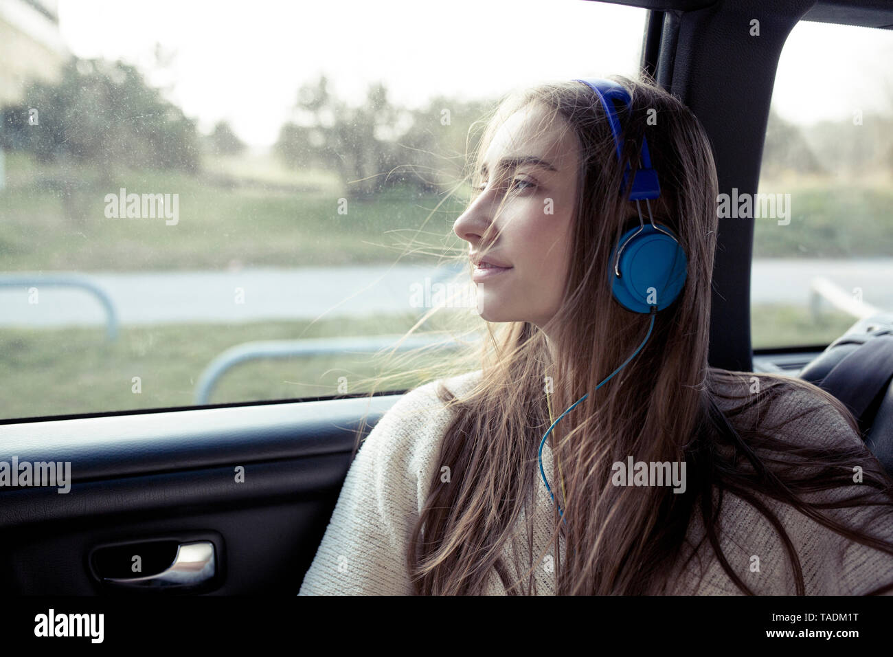 Giovane donna con capelli spazzate dal vento in un auto che indossano le cuffie Foto Stock
