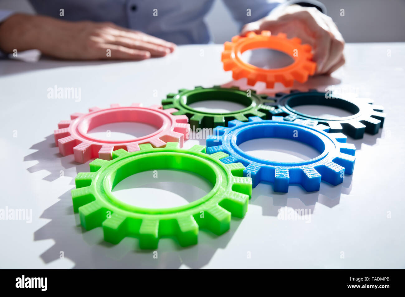 Imprenditore unendo insieme ingranaggi sul tavolo di legno al posto di lavoro Foto Stock