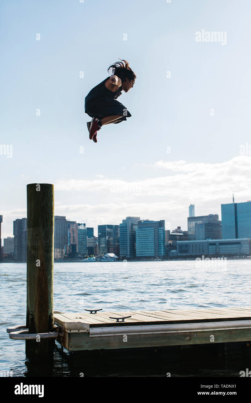 Stati Uniti d'America, New York, Brooklyn, il giovane uomo che fa parkour saltare da un palo di legno nella parte anteriore dello skyline di Manhattan Foto Stock