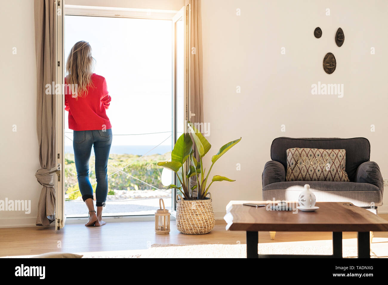 Vista posteriore della donna appoggiata alla finestra aperta a casa guardando il mare Foto Stock