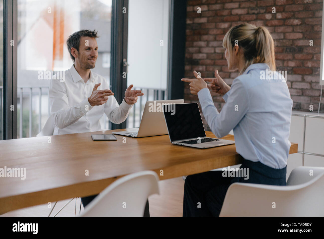 Imprenditore e donna seduta alla scrivania, lavorando su laptop, indicando con le dita a pistola a ciascun altro Foto Stock