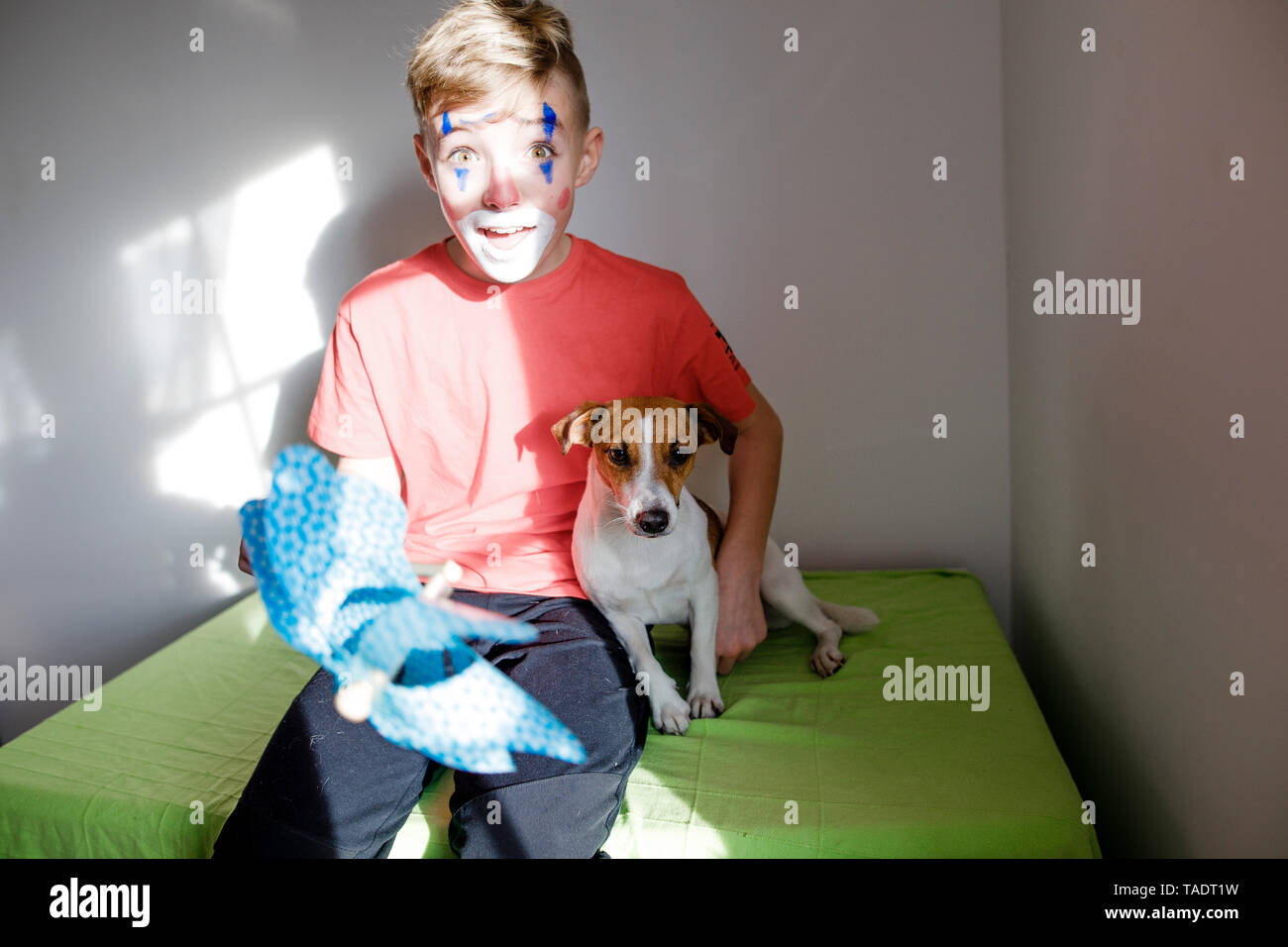 Ritratto di ragazzo stupito costituito come un clown con il cane e il perno ruota a casa Foto Stock