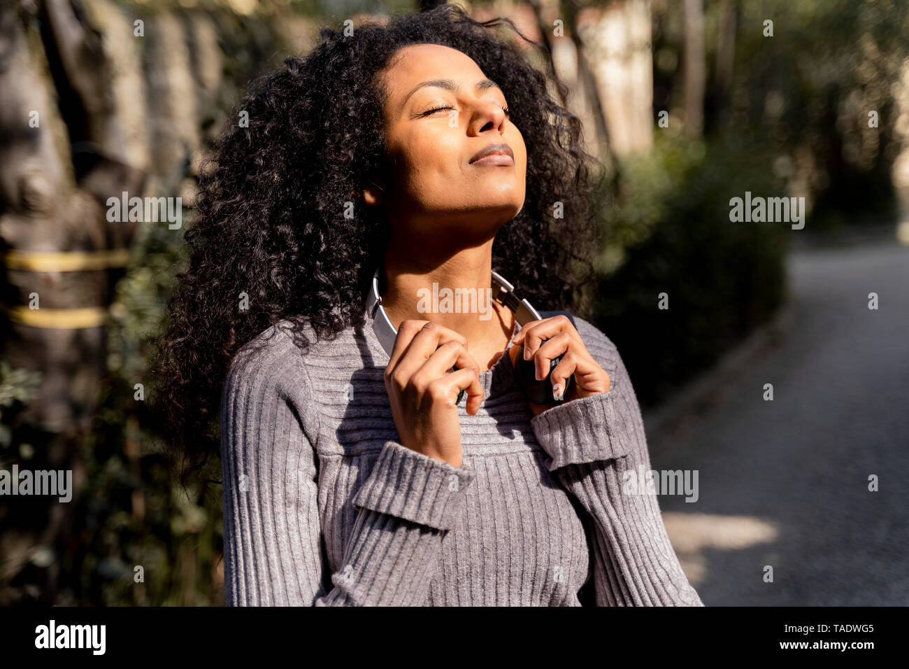 Ritratto di una donna con le cuffie, godersi il sole con gli occhi chiusi Foto Stock