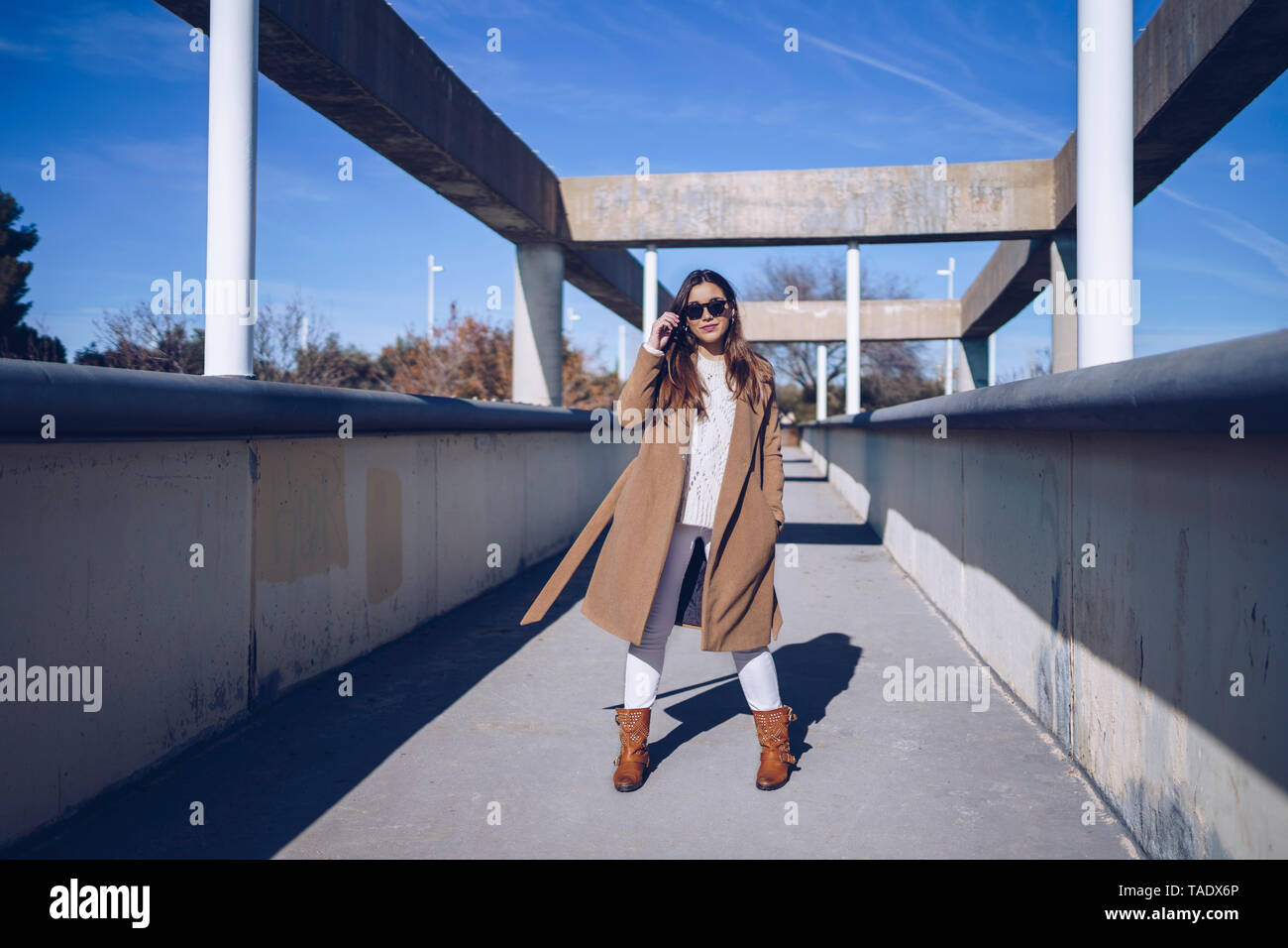 Giovane donna indossa cappotto e occhiali da sole in piedi su un ponte Foto Stock