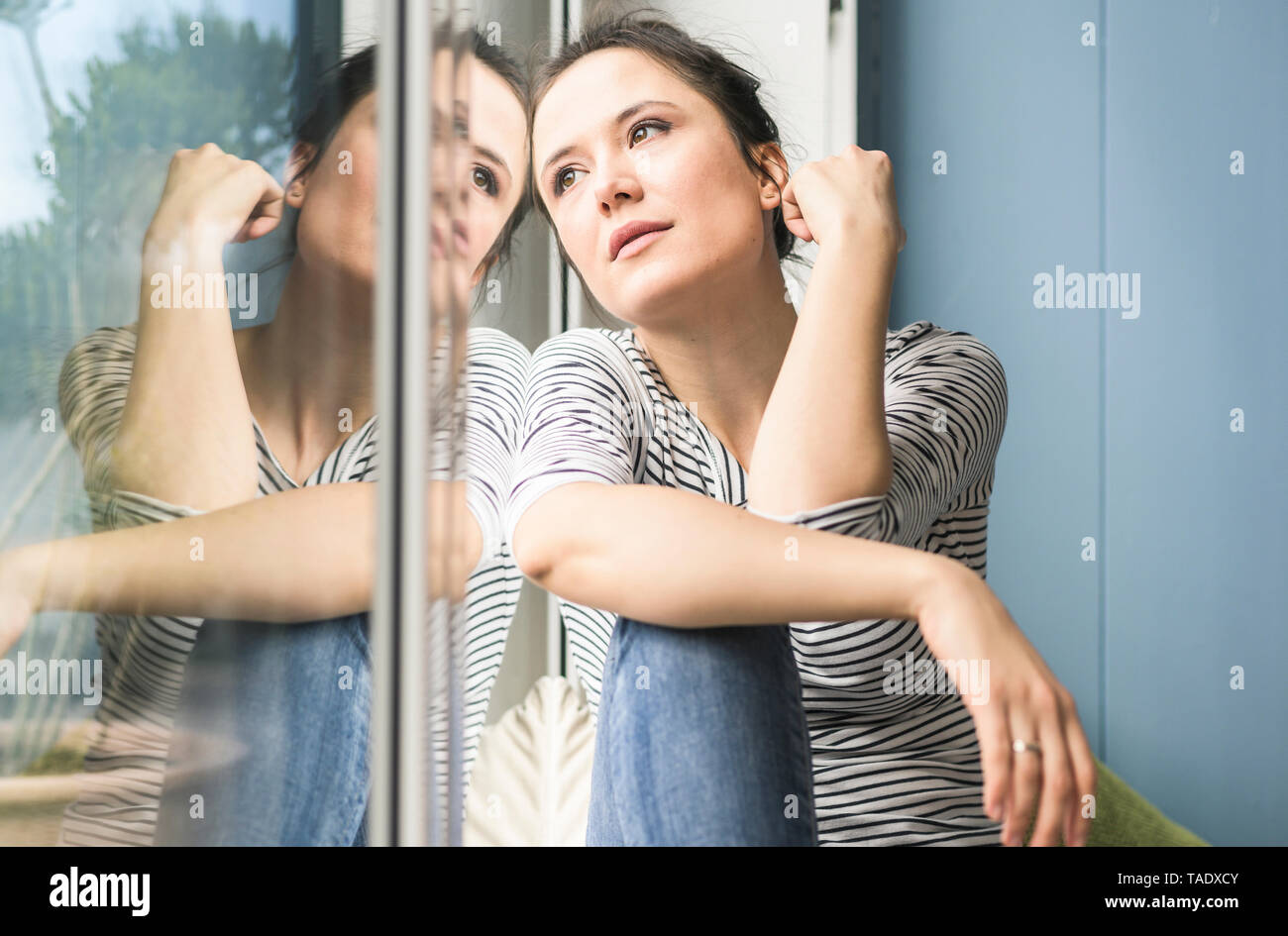 Grave donna guardando fuori della finestra a casa Foto Stock