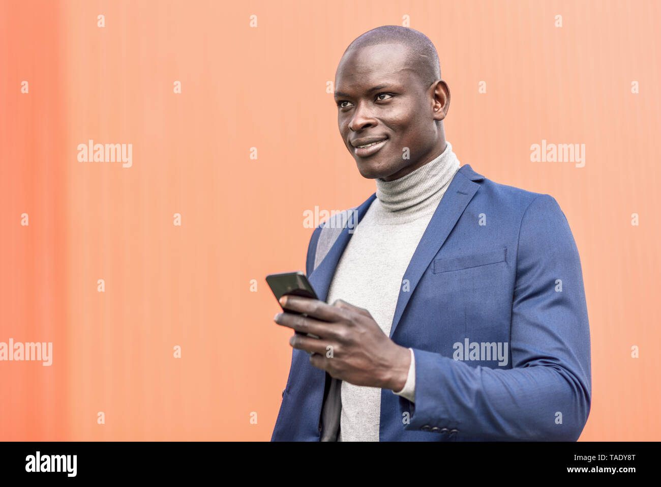 Ritratto di imprenditore sorridente con lo smartphone nella parte anteriore della parete arancione Foto Stock