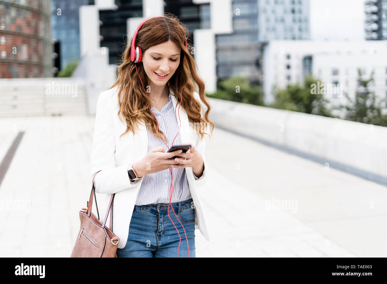 Giovane imprenditrice pendolarismo nella città, utilizza lo smartphone e le cuffie Foto Stock