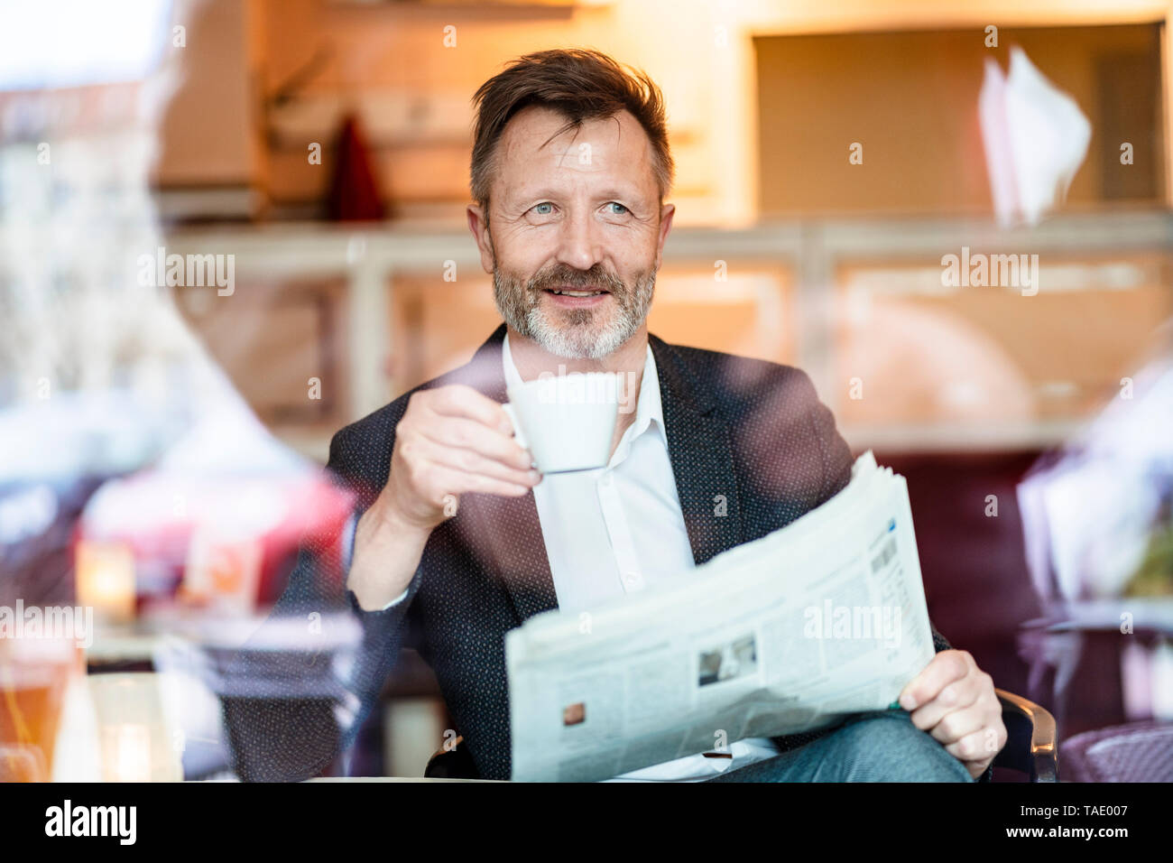 Ritratto di sorridente imprenditore maturo con quotidiano seduti in un caffè a bere caffè Foto Stock