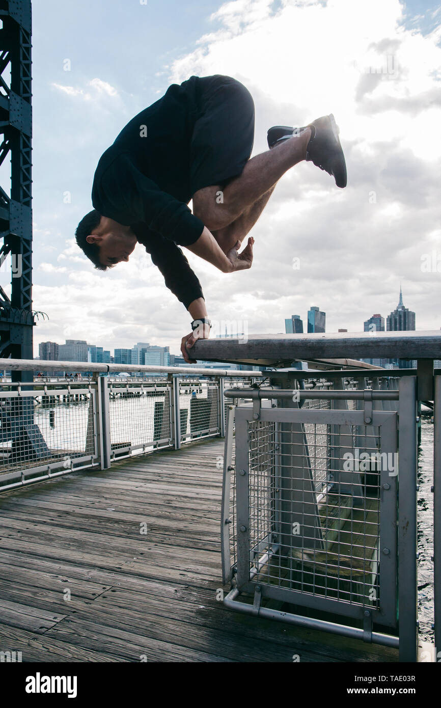 Stati Uniti d'America, New York, Brooklyn, il giovane uomo che fa parkour handstand sulla ringhiera del molo di fronte skyline di Manhattan Foto Stock