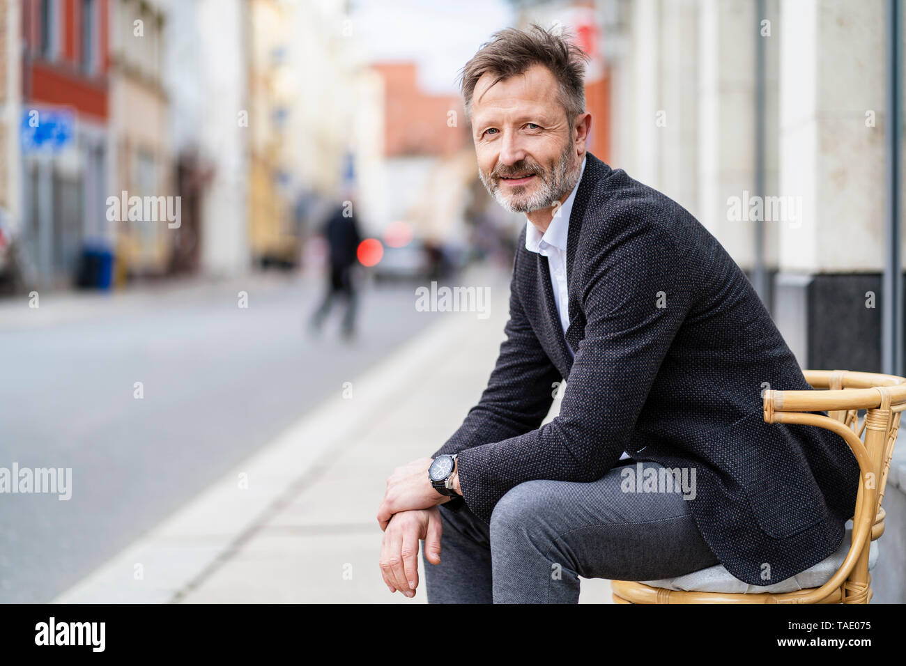 Ritratto di sorridente imprenditore maturo seduto su una sedia nella città Foto Stock